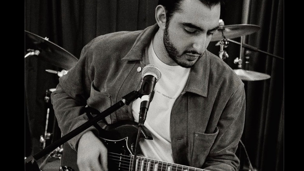 Hayk playing electric guitar and singing into a microphone in a black-and-white photograph